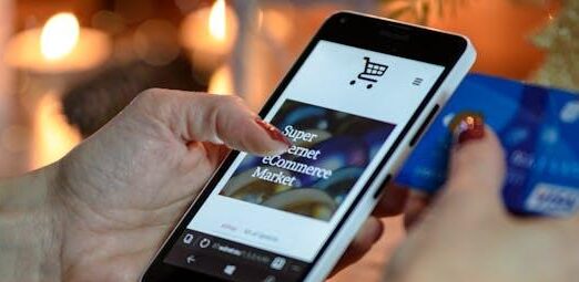 Woman using smartphone for online shopping with credit card in hand, festive background lighting.